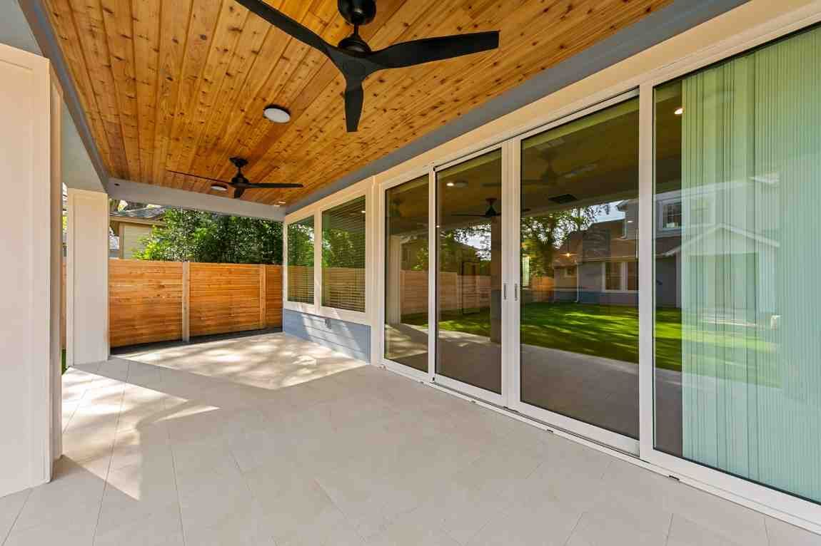 Covered patio with sliding glass doors, wood ceiling, and ceiling fans overlooking a backyard with green grass.