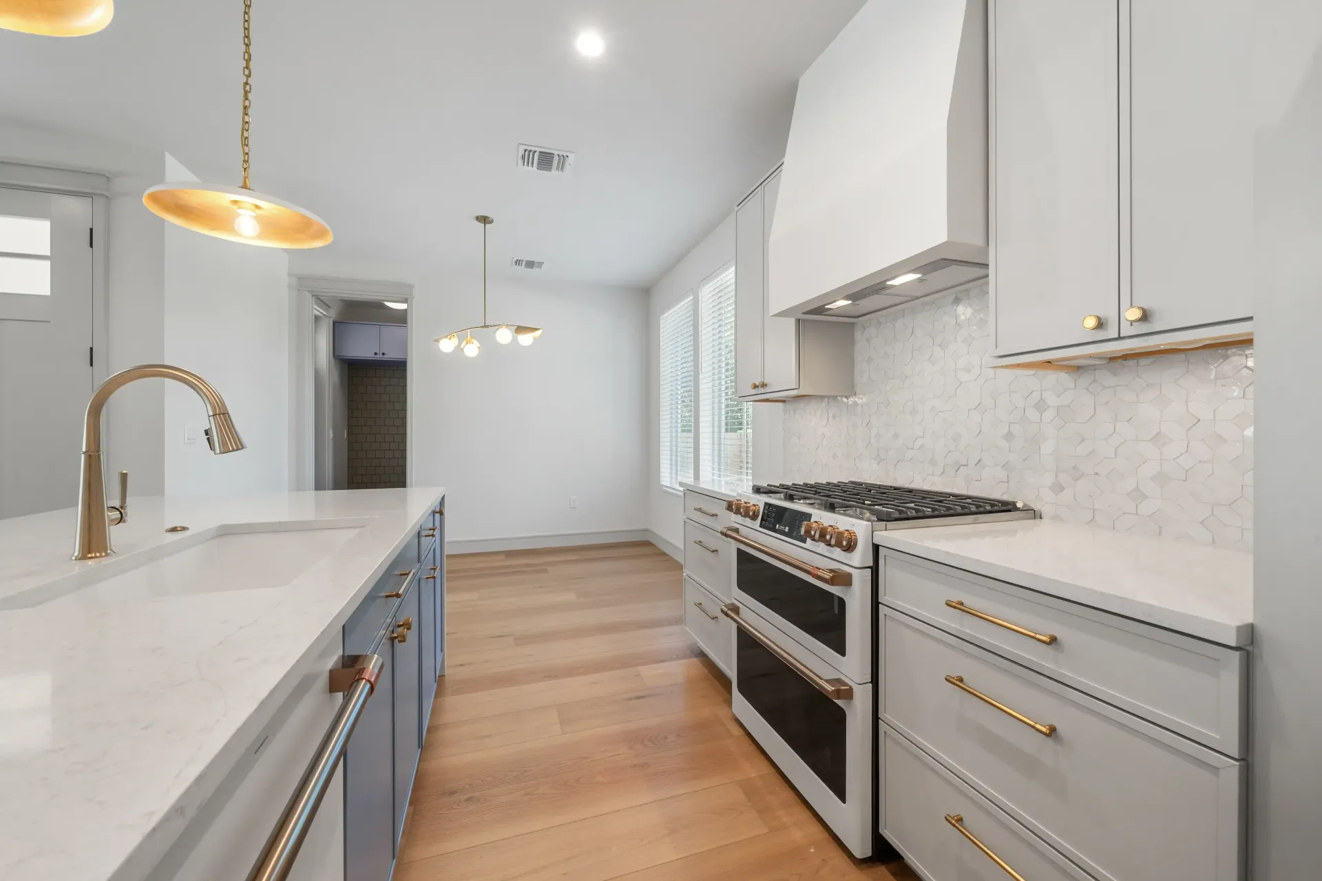 Modern kitchen with white cabinetry, gold fixtures, and a large stovetop.