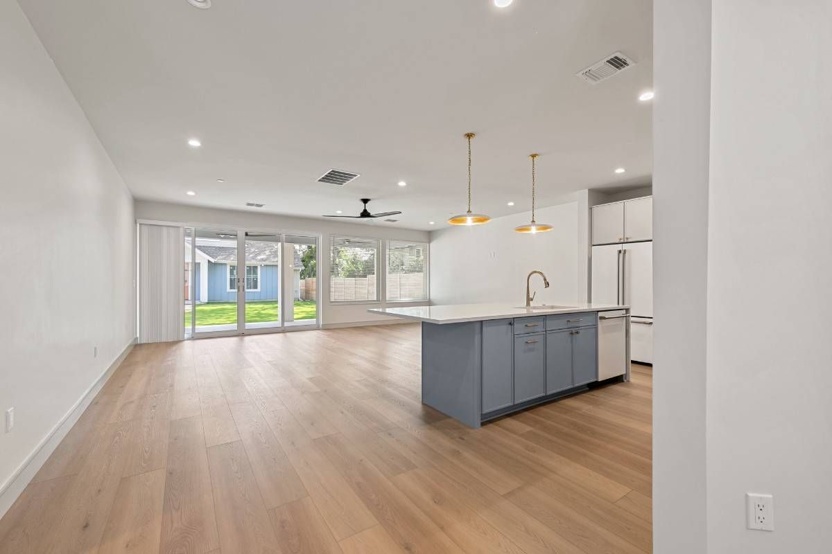 Spacious open-concept living space with hardwood floors, kitchen island, and sliding glass doors to a backyard.