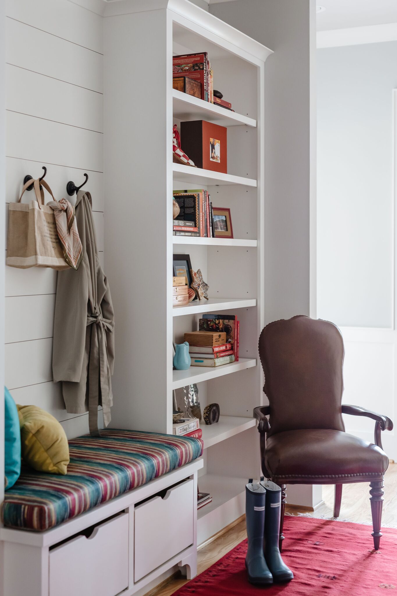 A hallway with a bench , chair , shelves and boots.