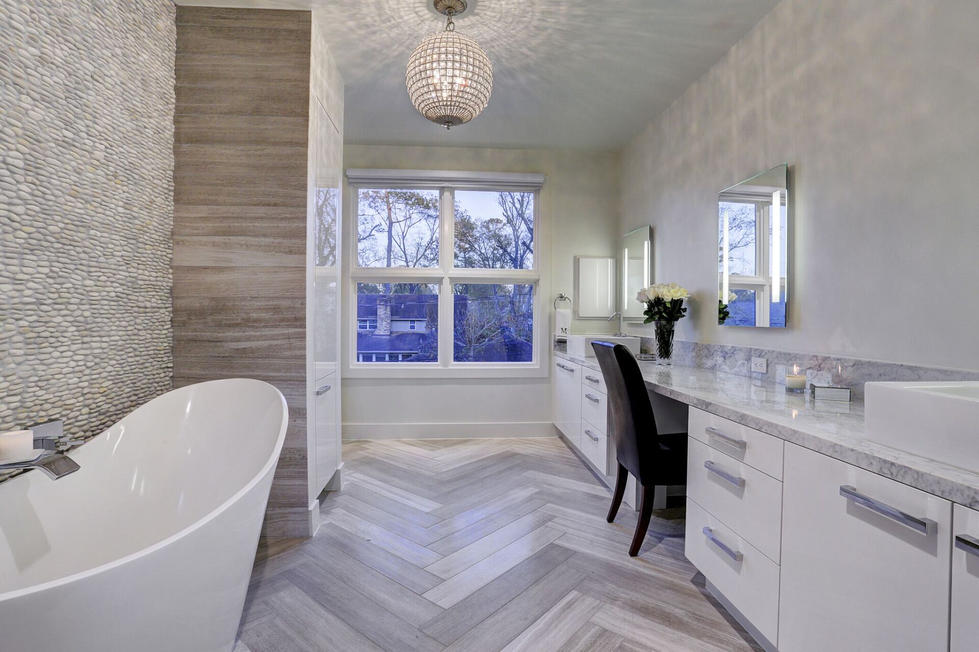 A bathroom with a tub , sink , mirror , and chair.