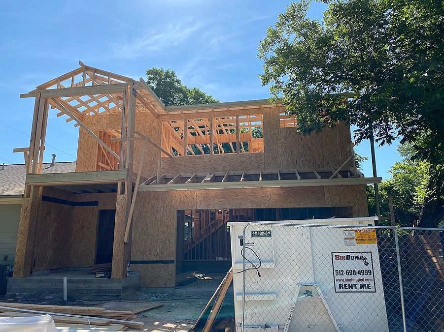 A house is being built with a white dumpster in front of it.