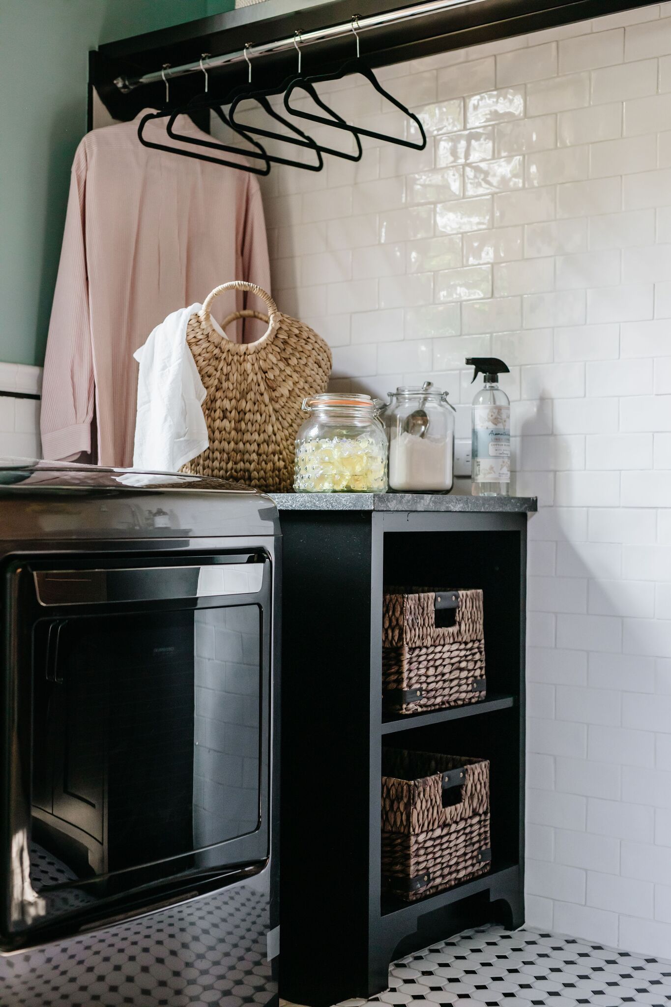 A laundry room with a dishwasher , baskets , and clothes hanging on the wall.