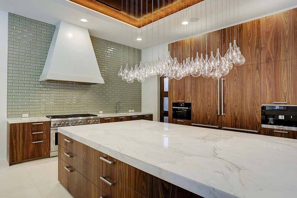 A kitchen with wooden cabinets , a large island , a stove and a chandelier hanging from the ceiling.
