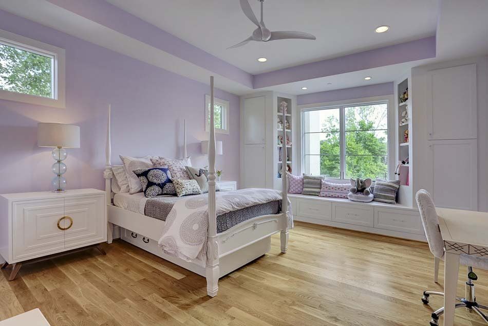 A bedroom with purple walls , a four poster bed , a desk , and a window seat.