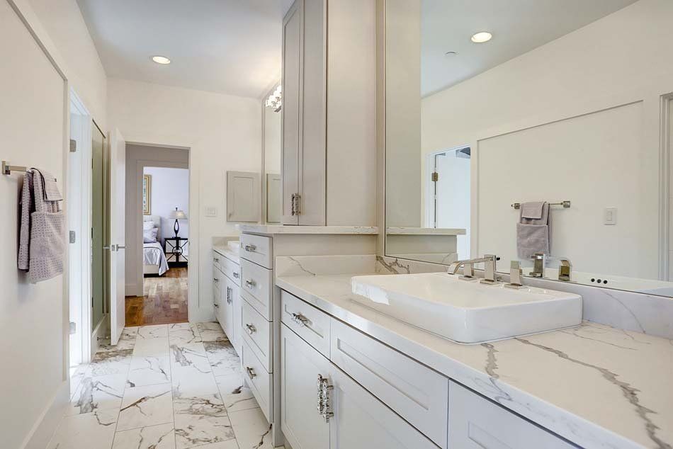 A bathroom with white cabinets , a sink , and a mirror.