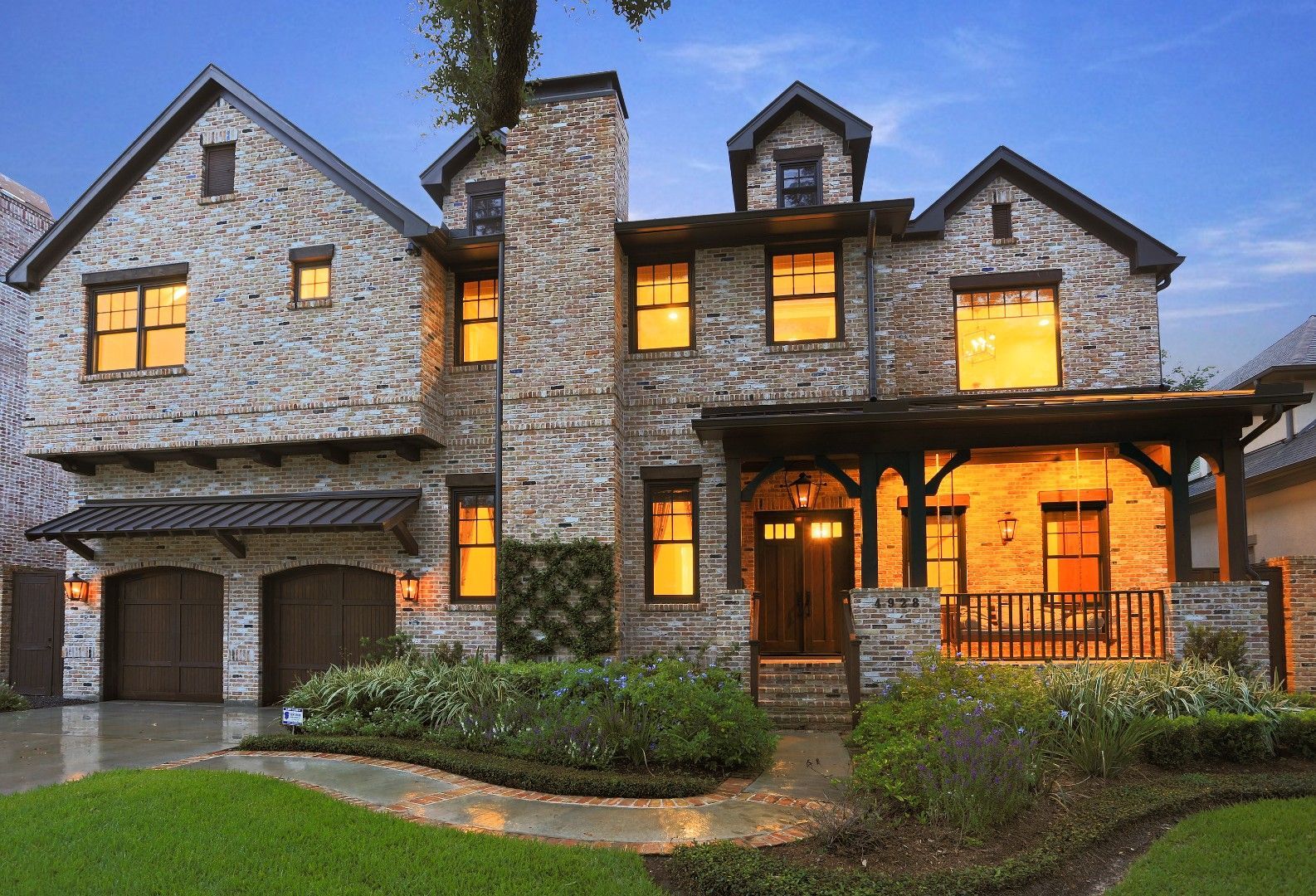 Two-story stone house with a porch, garage, and landscaping, illuminated at dusk.