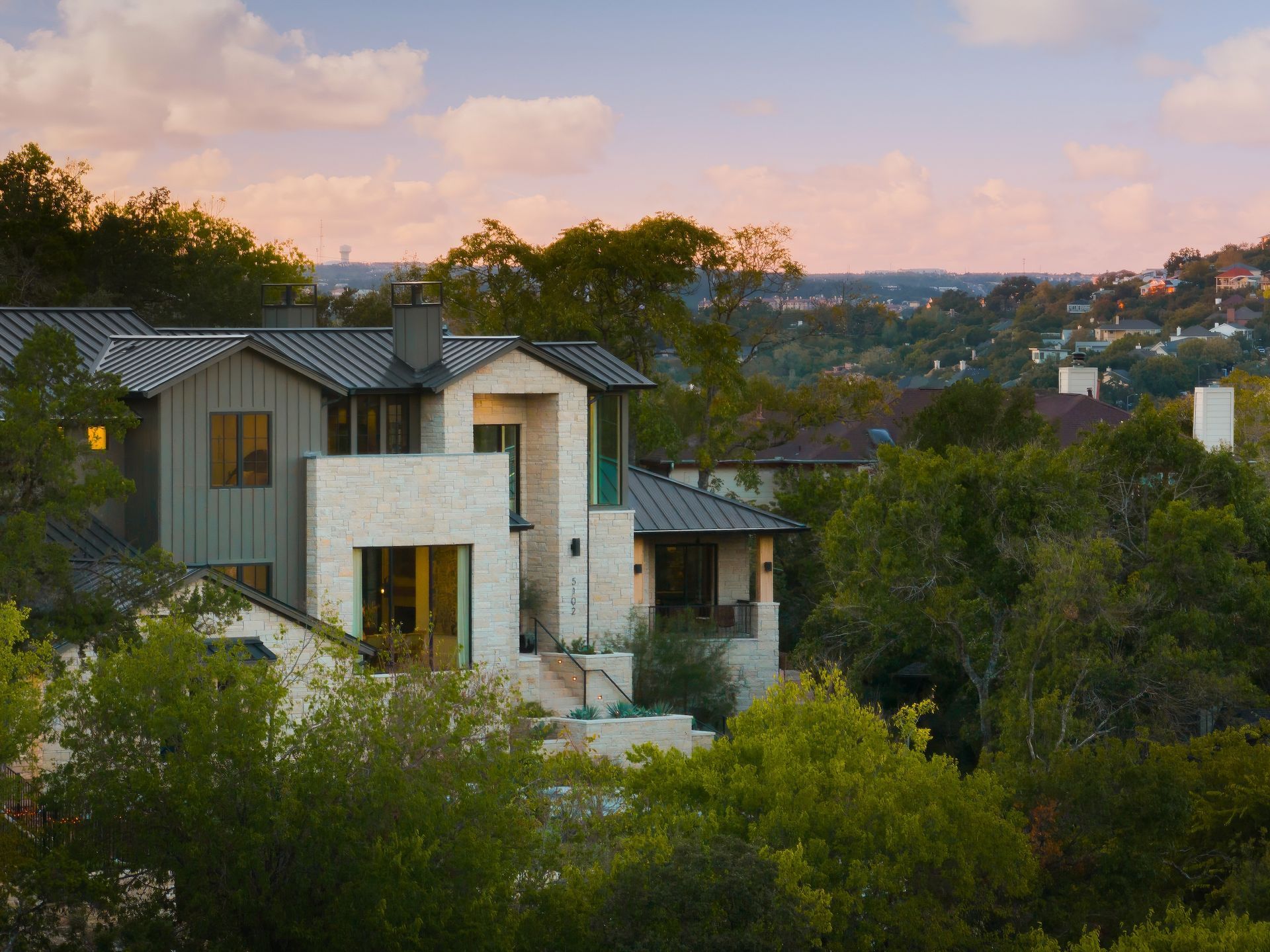 A large house sits on top of a hill surrounded by trees
