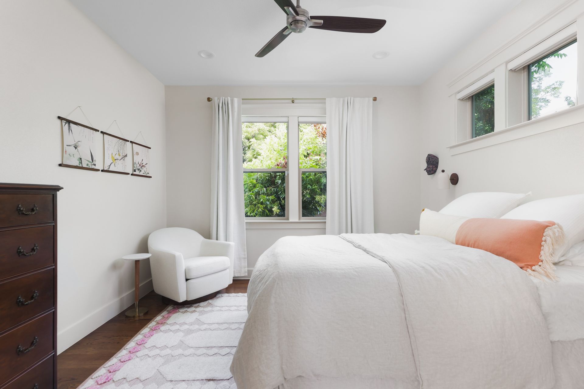 A bedroom with a bed , chair , dresser and ceiling fan.