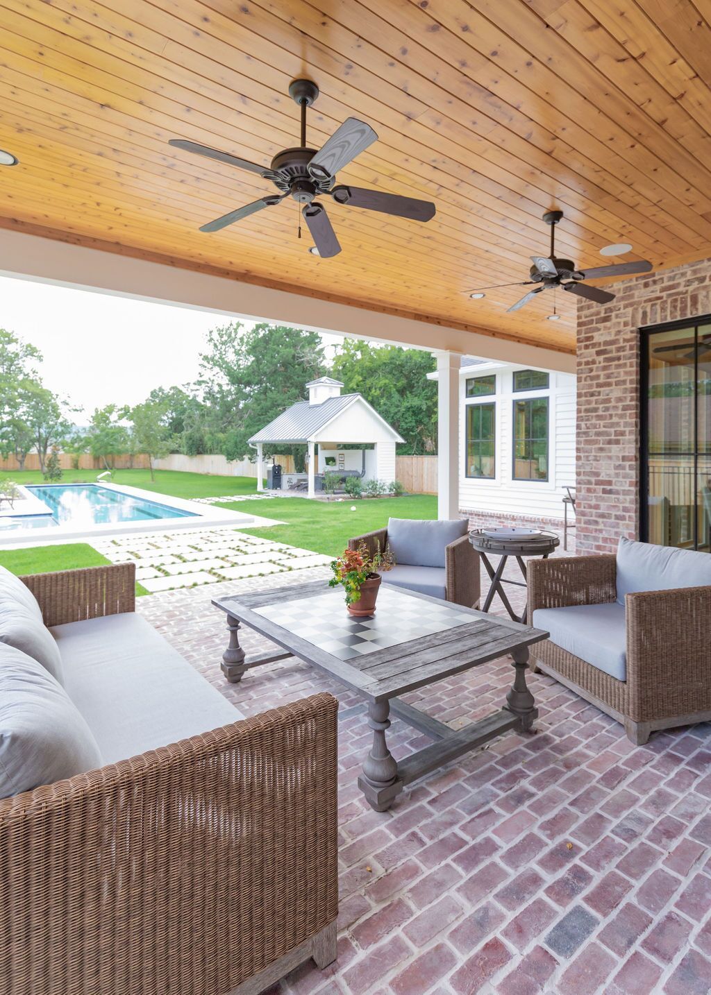 A patio with a couch , chairs , coffee table and ceiling fan.