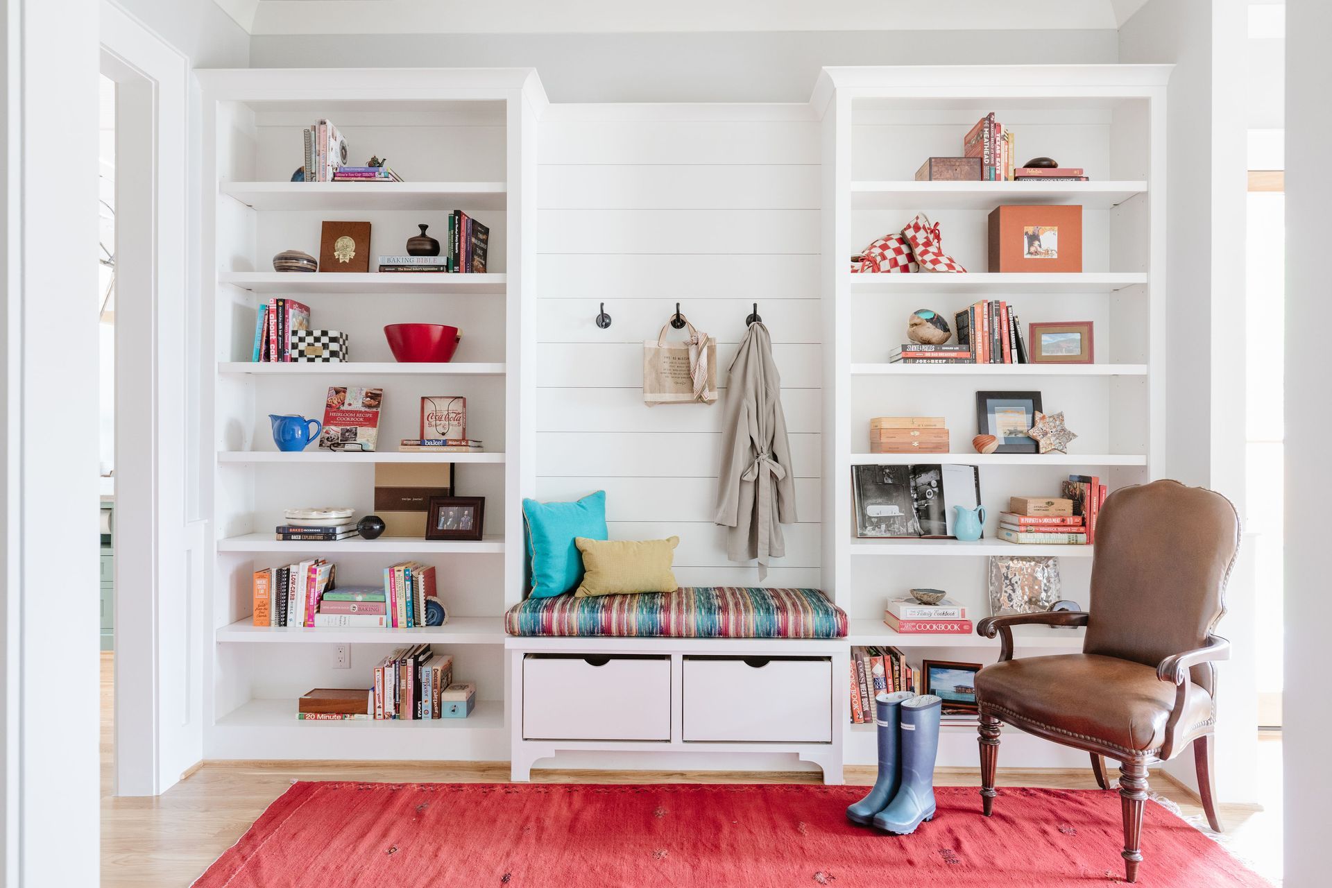 A hallway with a bench , chair , shelves and a rug.