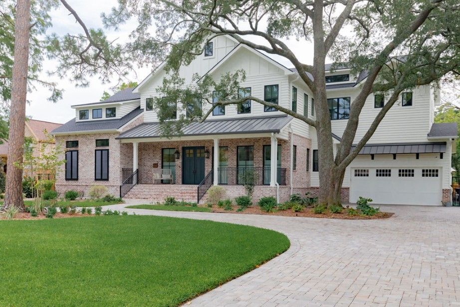 Two-story house with white siding, brick accents, black windows, and a large driveway, set in a grassy yard.