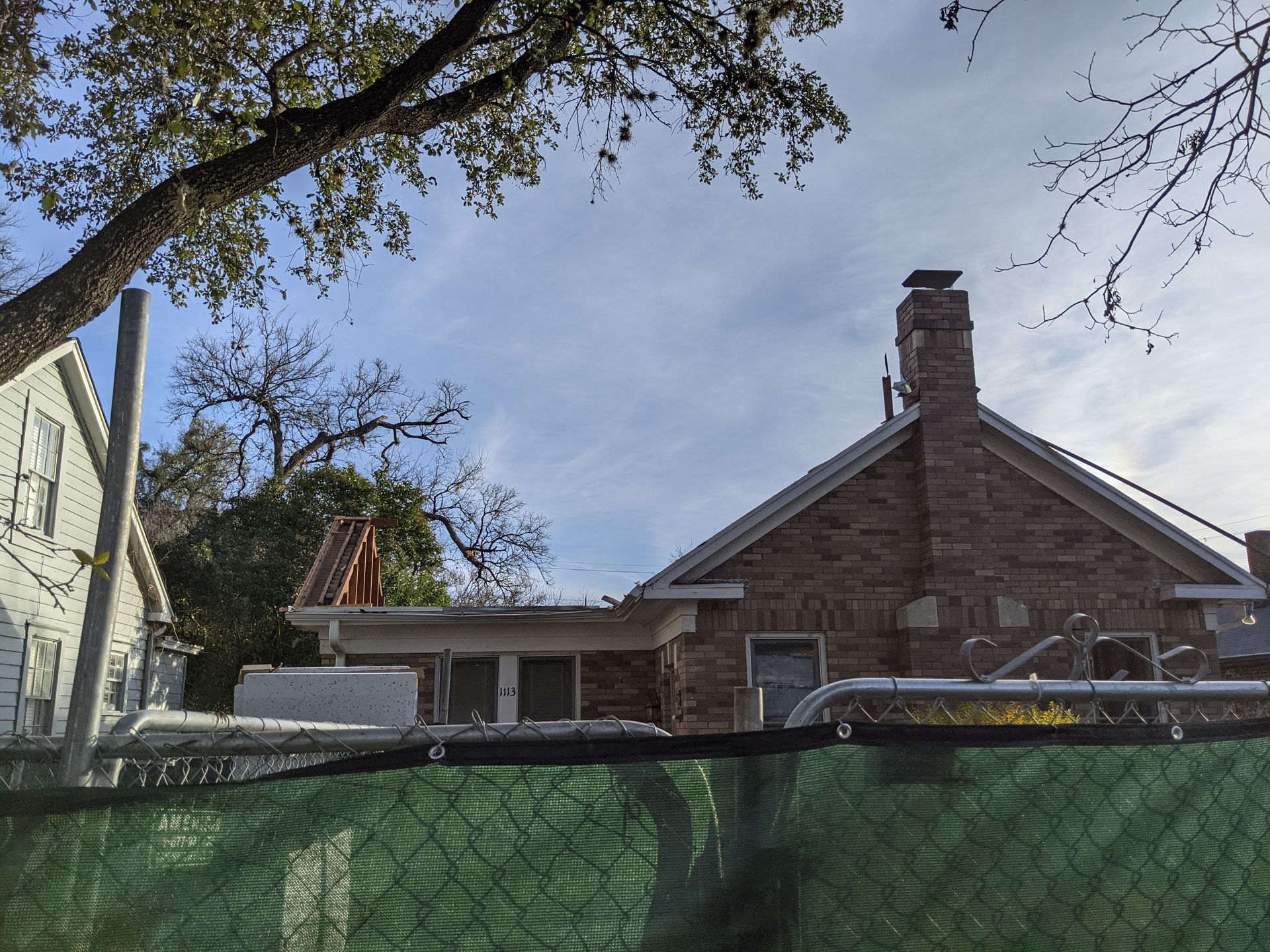 A brick house with a chimney is behind a chain link fence