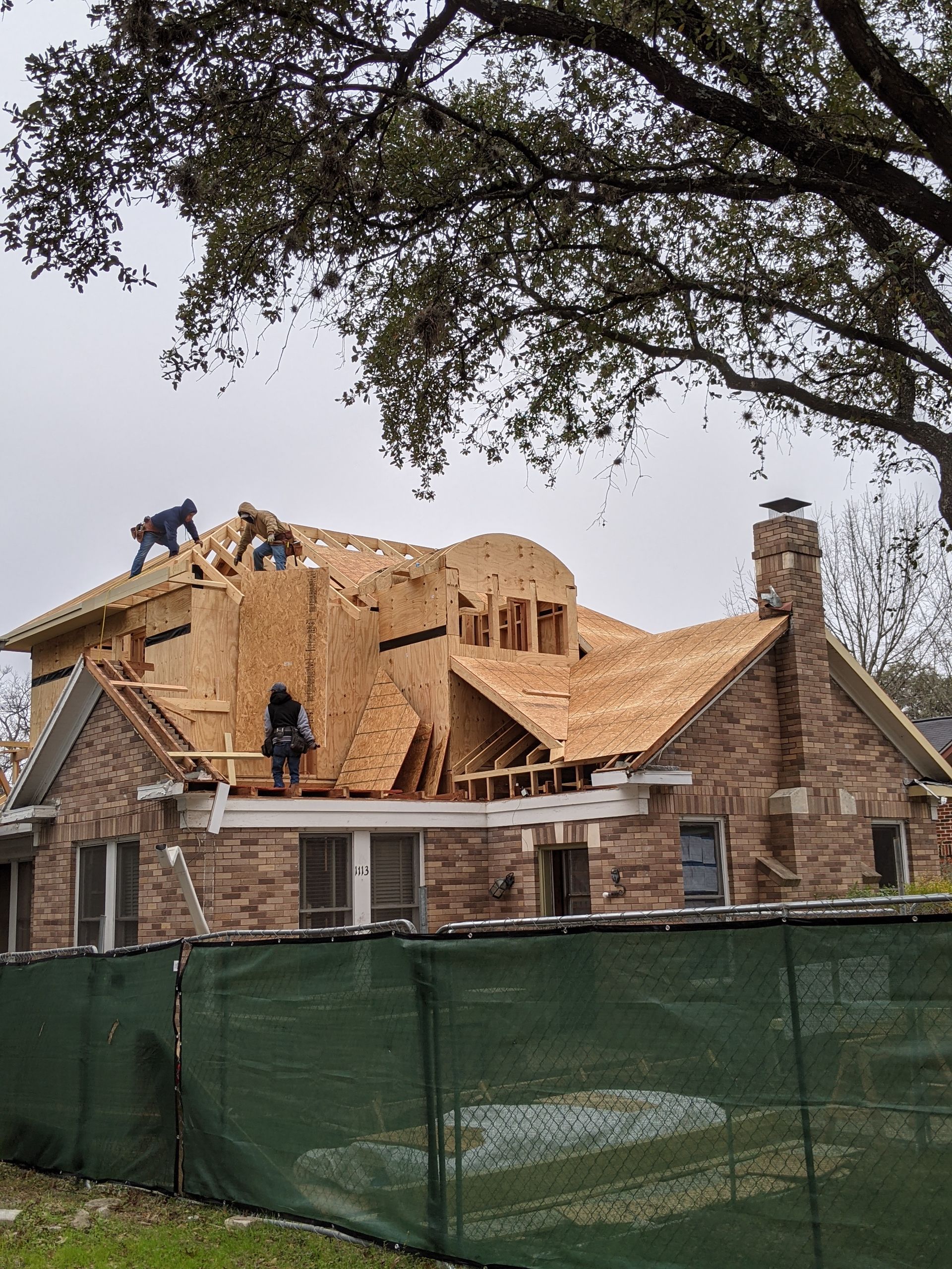 A large brick house is being built with a green fence in front of it.