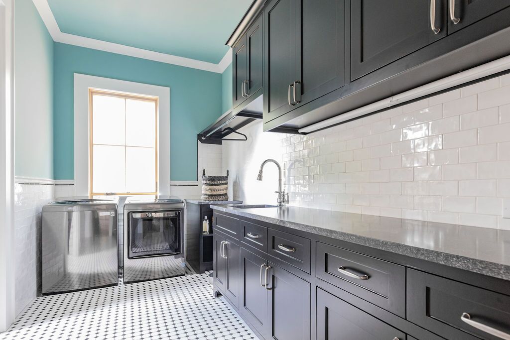A kitchen with black cabinets , stainless steel appliances , a sink , and a window.