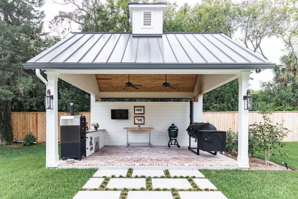 A white pavilion with a metal roof and a grill in the backyard.