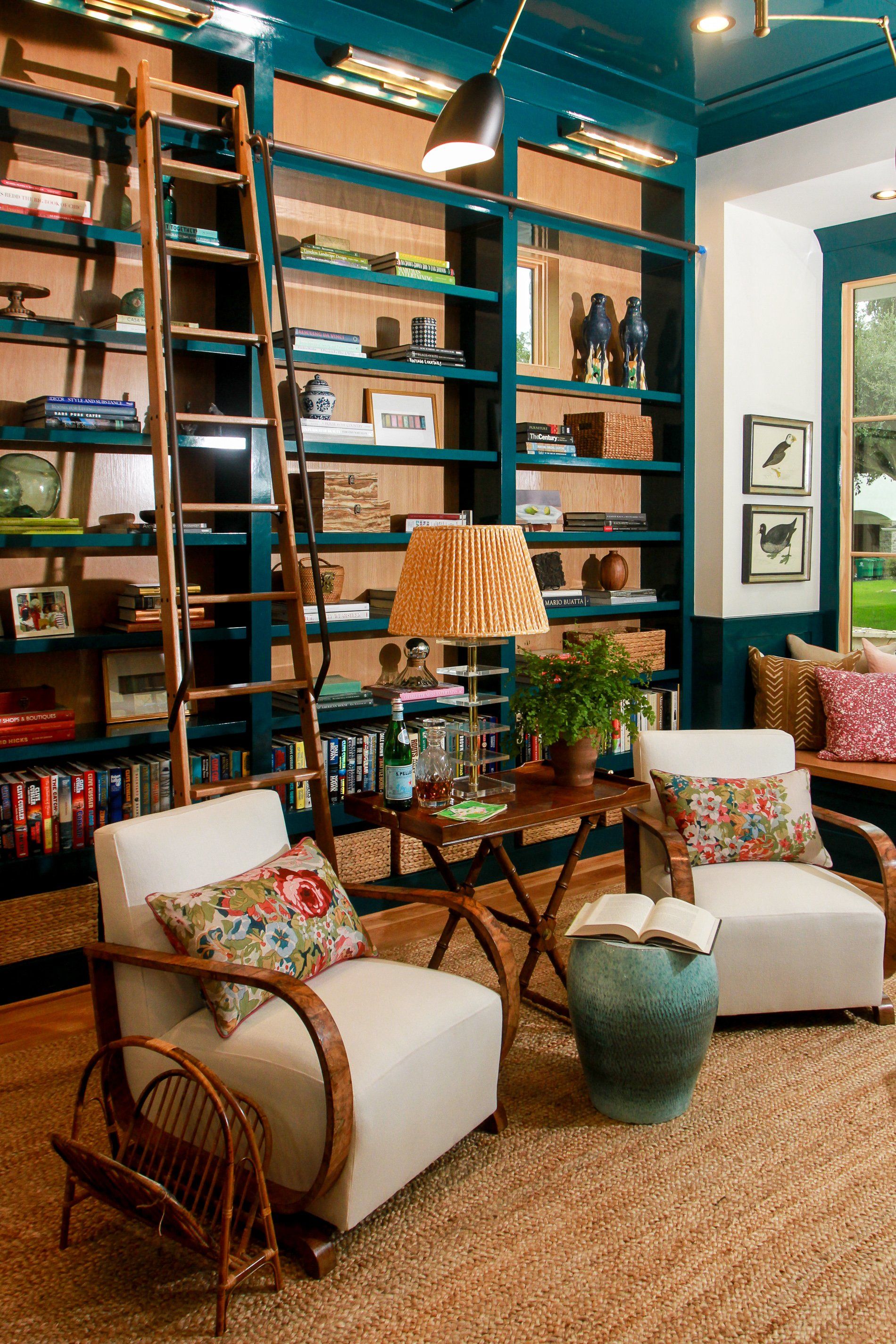 A living room with two chairs , a table , a lamp and a ladder.