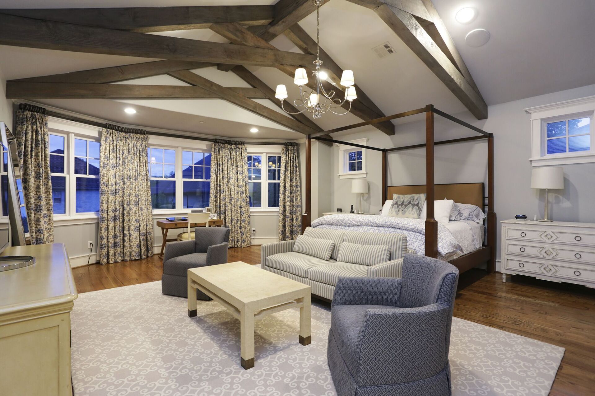 A large bedroom with a canopy bed , couch , chairs , coffee table and dresser.