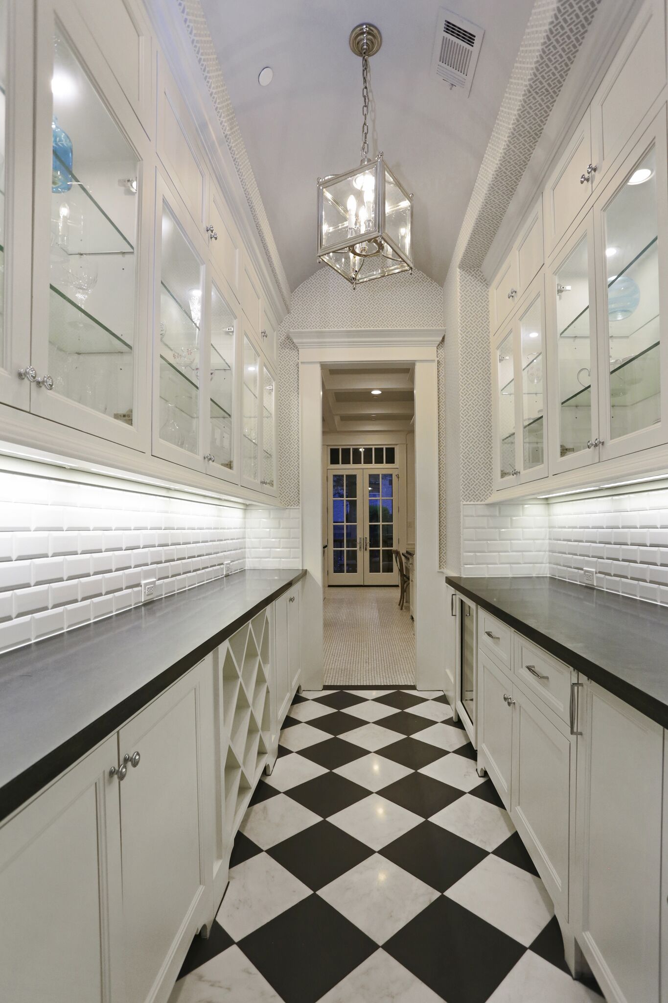 A long hallway with black and white checkered floors and white cabinets.