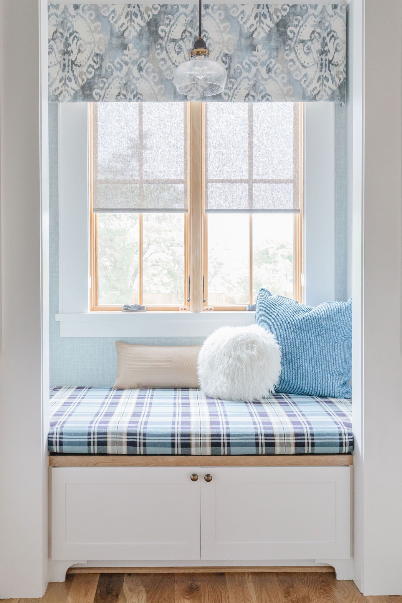 A window seat with a blue and white plaid cushion and pillows.