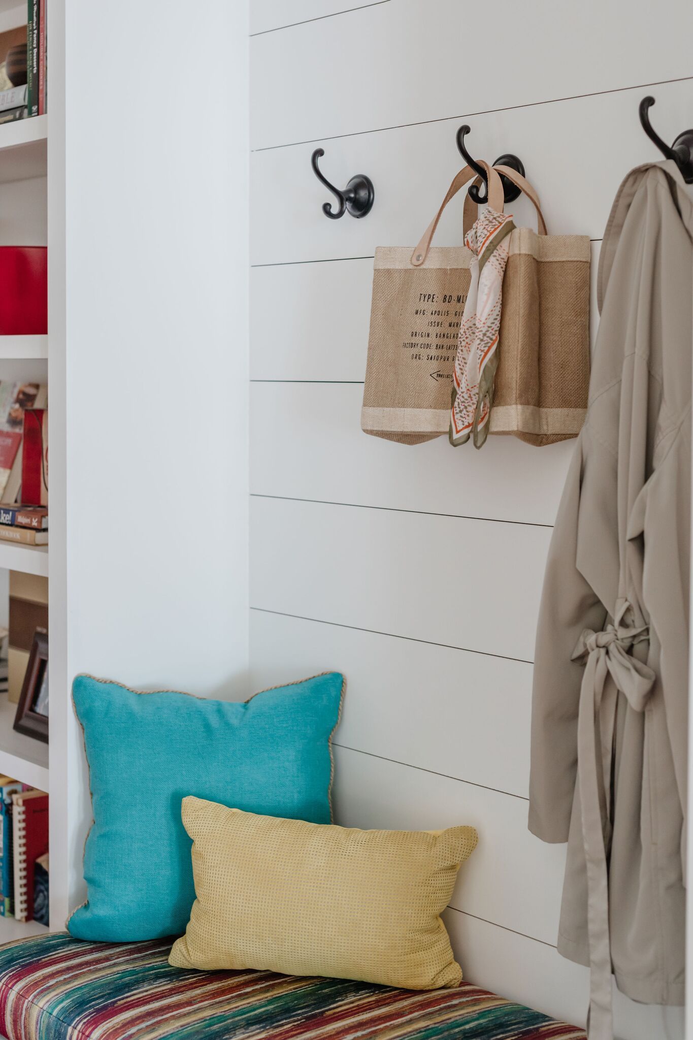 A corner of a room with pillows and a coat hanging on hooks.