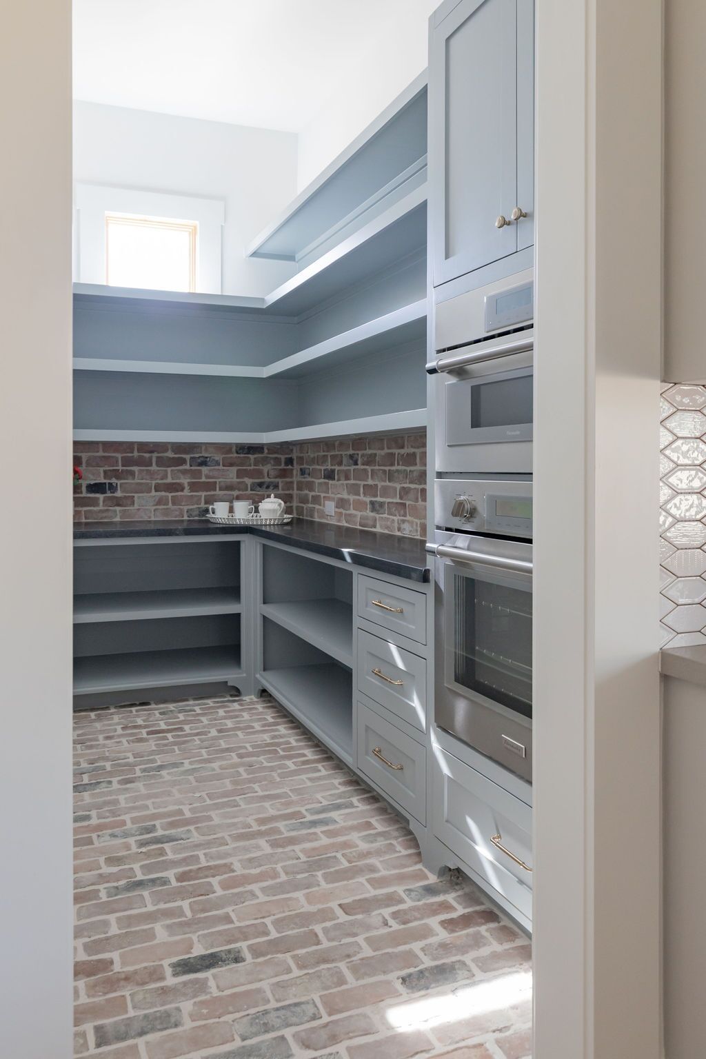 A kitchen with brick floors , gray cabinets , and stainless steel appliances.