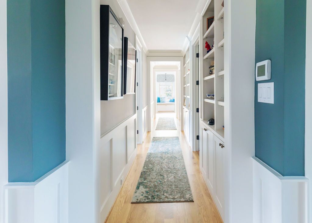 A long hallway with blue walls and white cabinets leading to a living room.