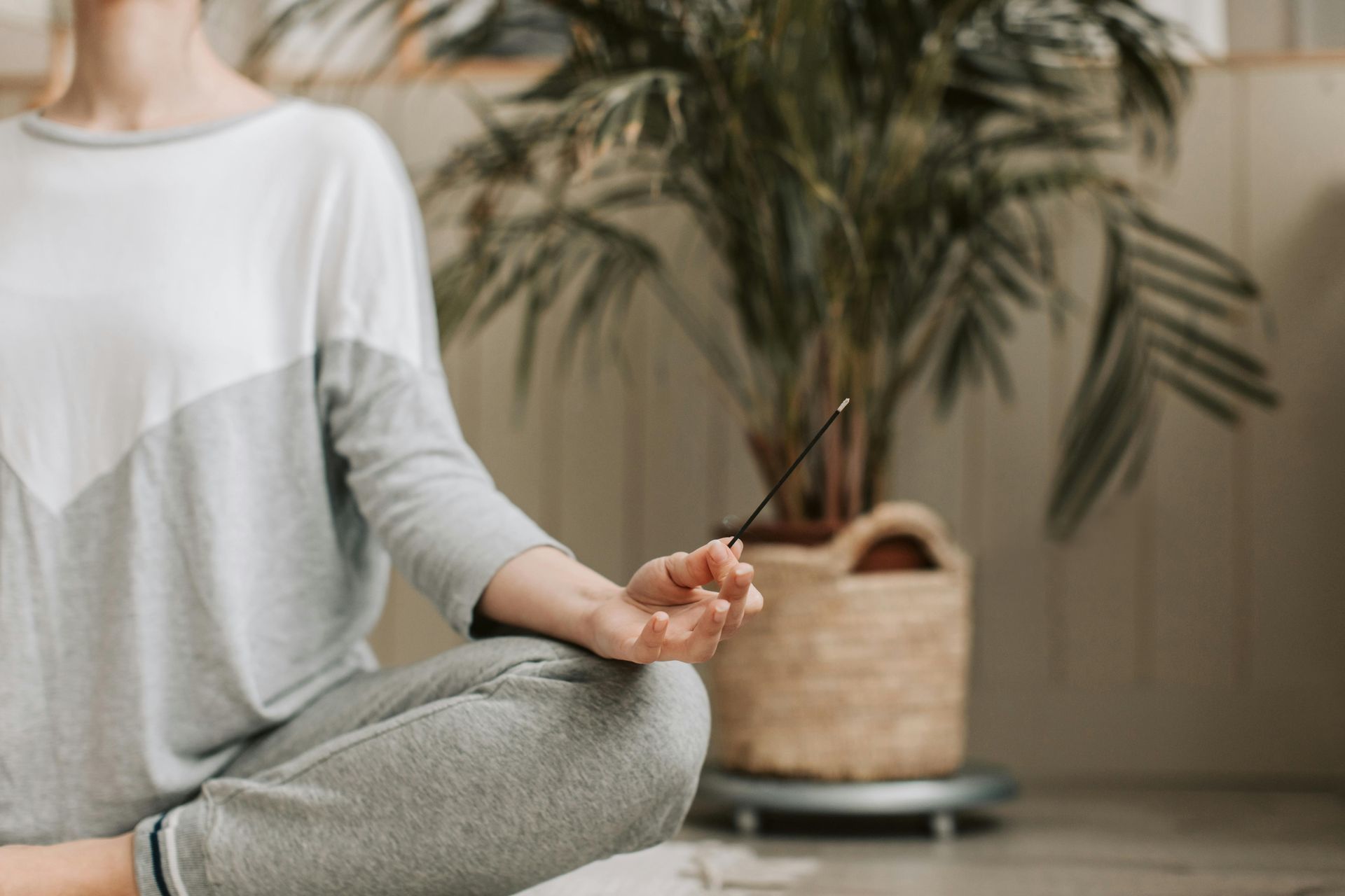 Person in yoga pose holding incense near a potted plant.