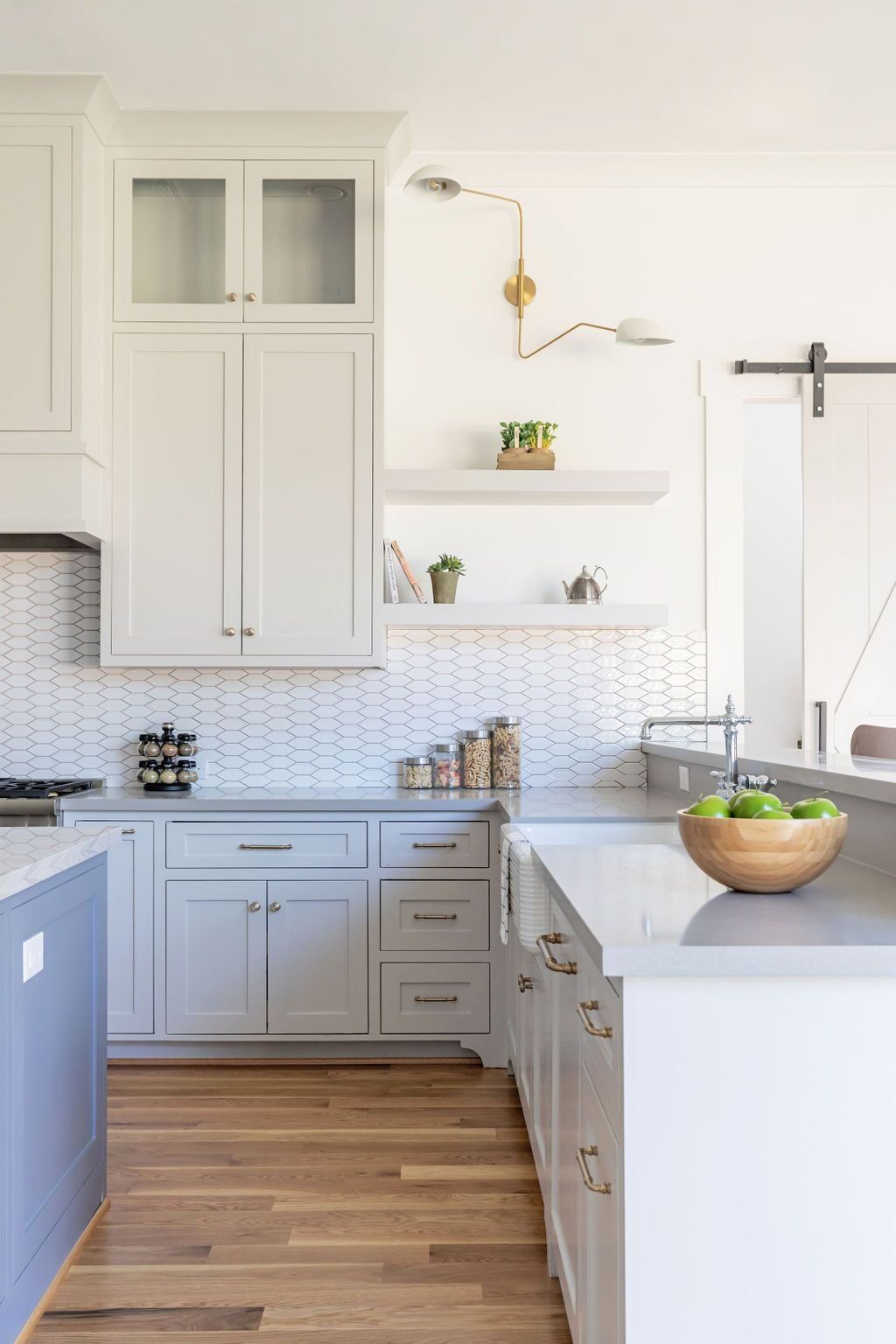 A kitchen with white cabinets and wooden floors and a bowl of apples on the counter.