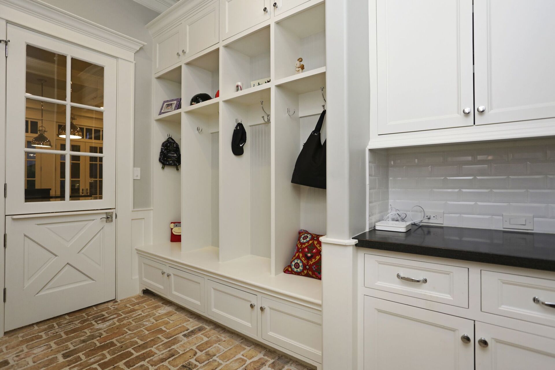 A mud room with white cabinets and a brick floor