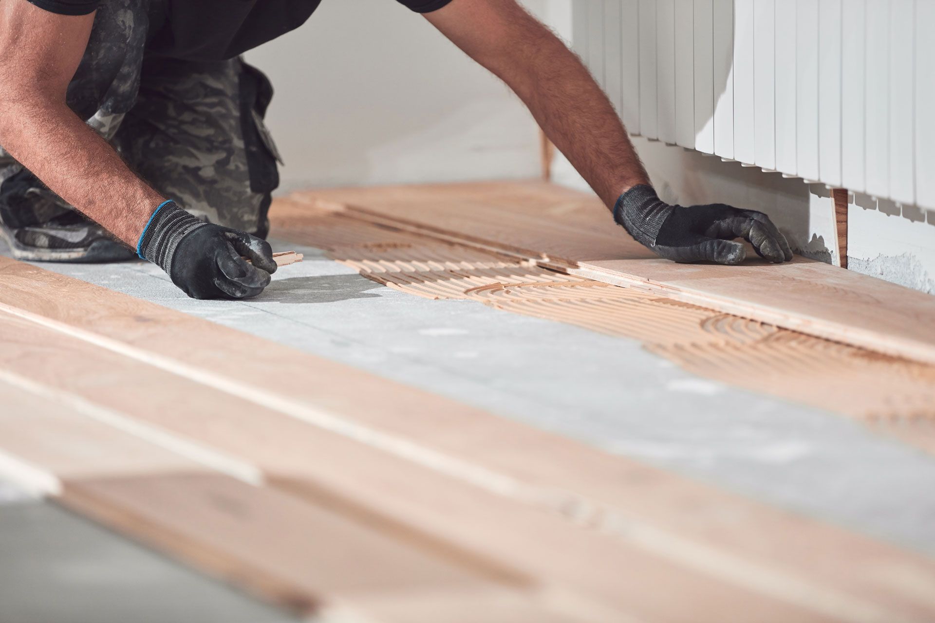 Worker installing wooden floorboards with glue in a room under renovation
