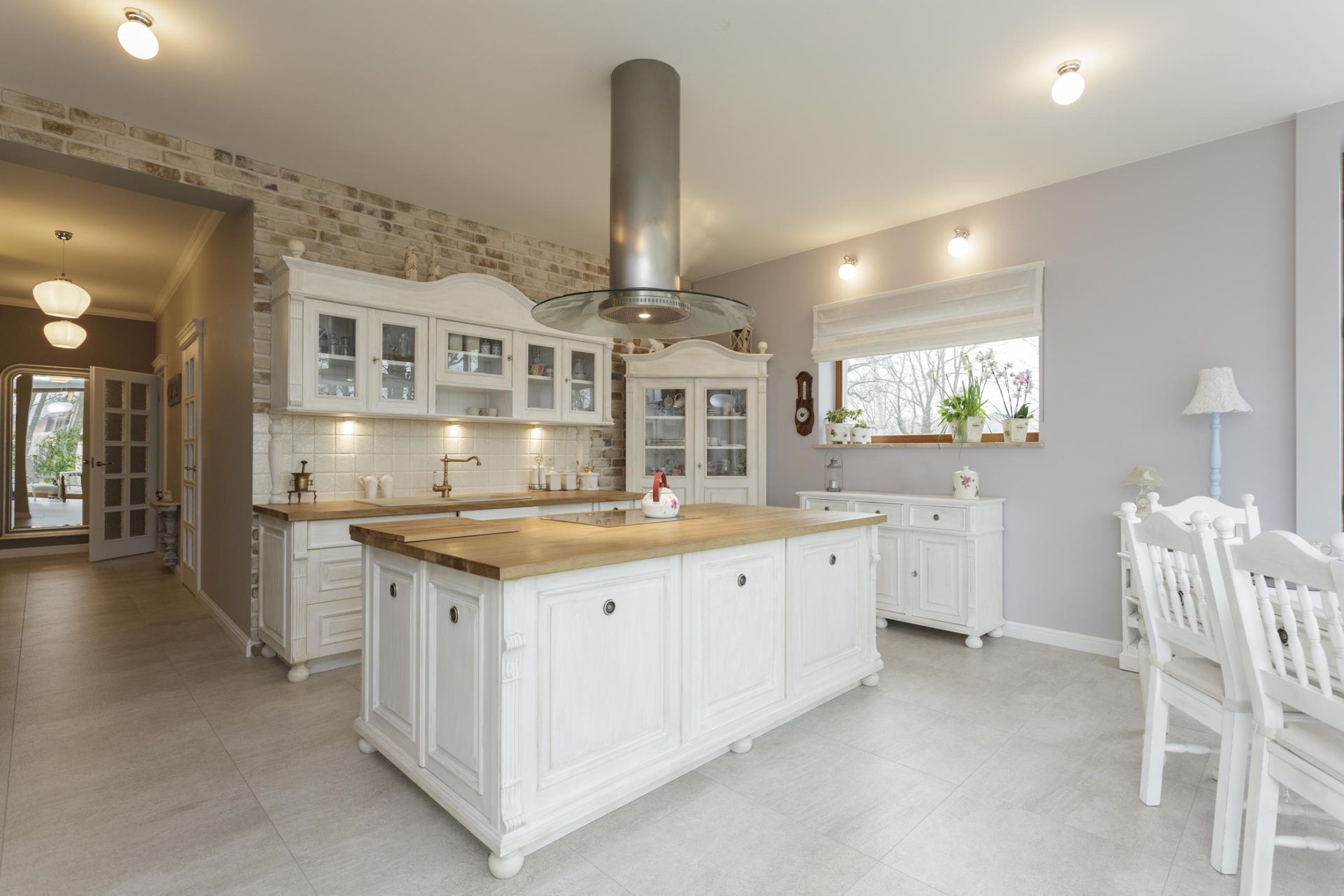 Bright white farmhouse kitchen with island, wood countertops, and dining area by a window