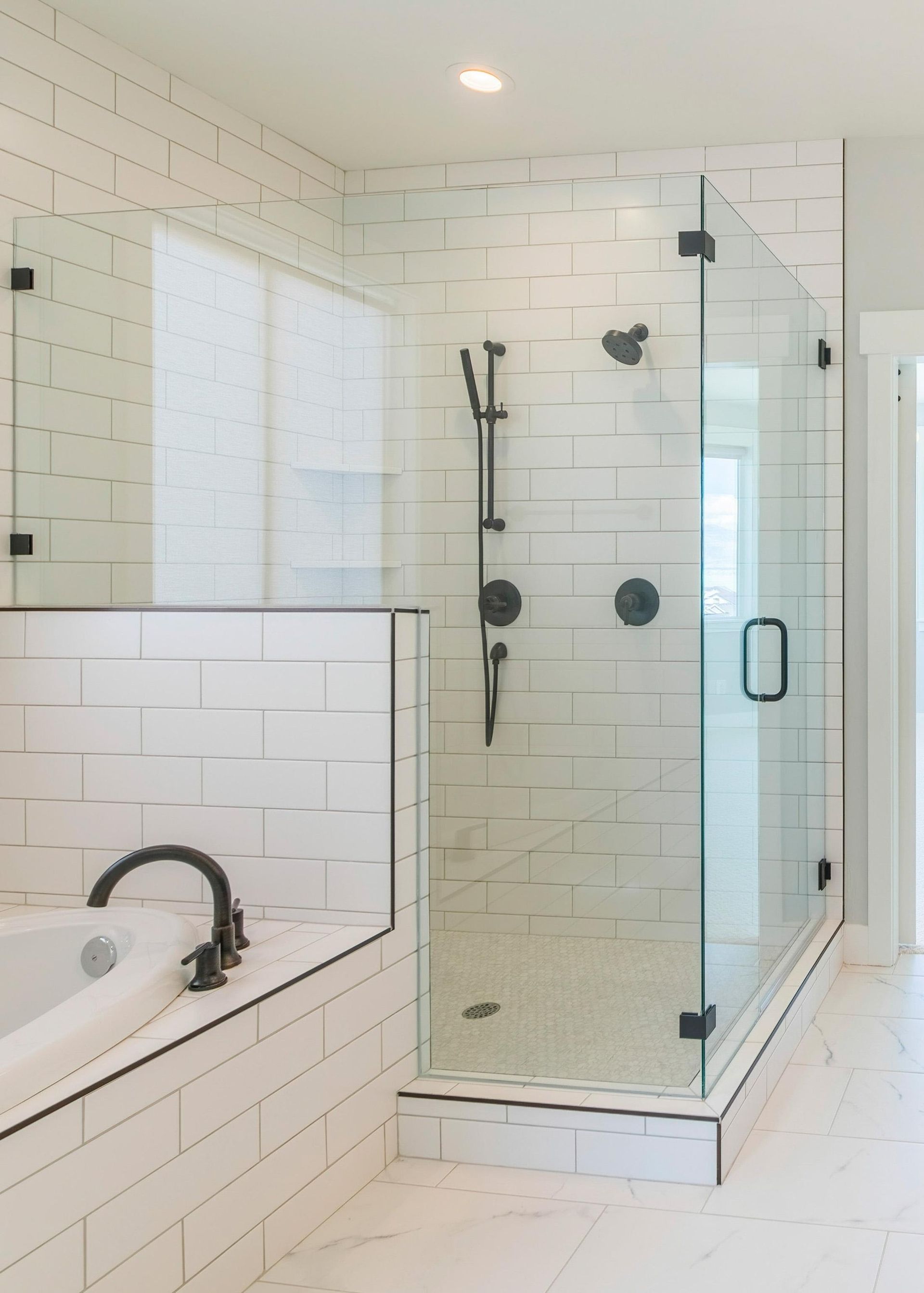 Modern white-tiled bathroom with glass-enclosed shower and bathtub divider