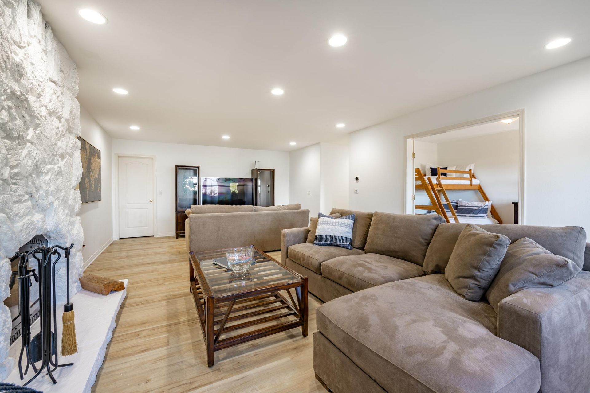 Bright living room with gray sectional sofa, wooden coffee table, stone fireplace, and recessed ceiling lights
