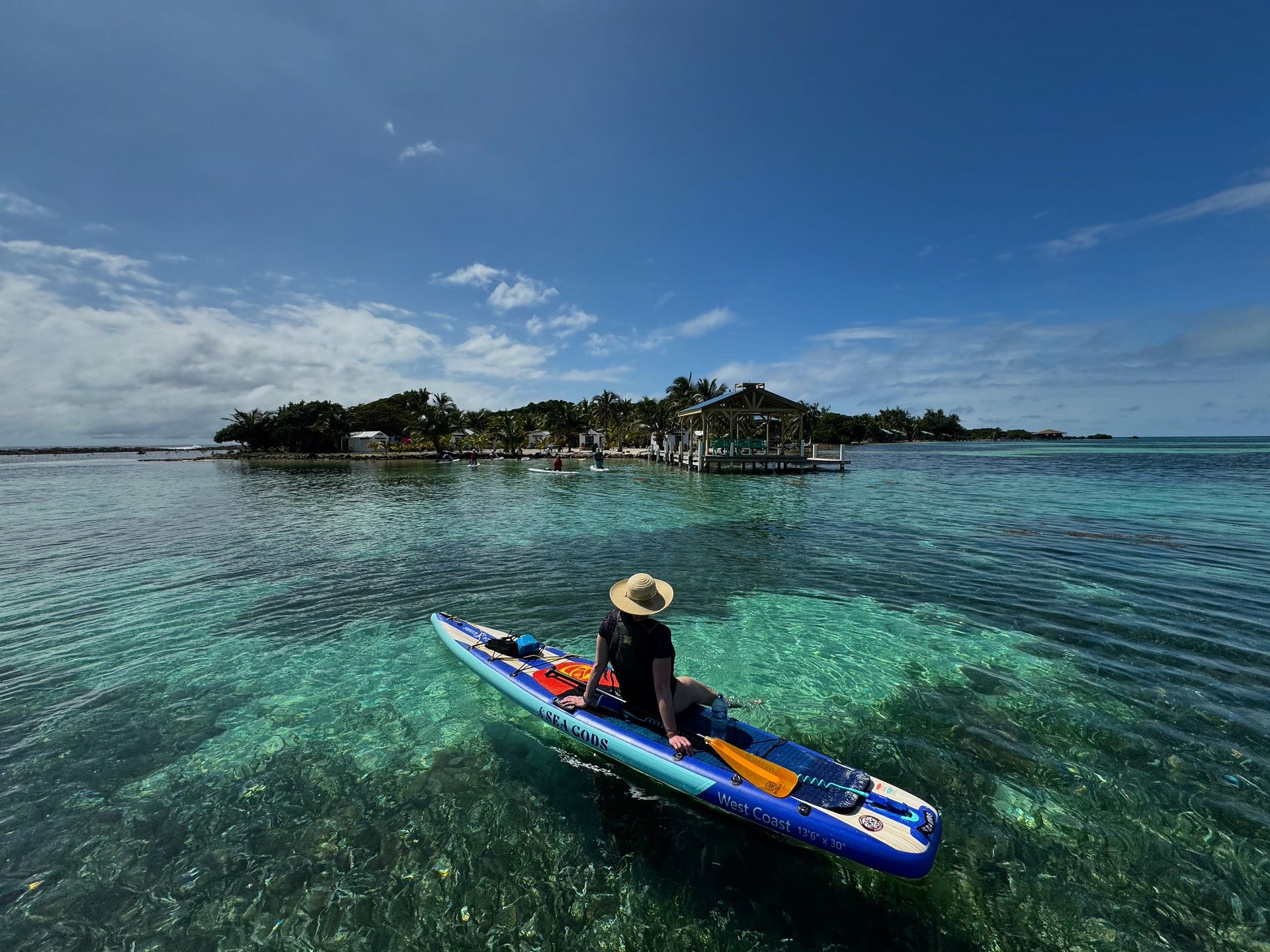 Person kayaking on clear turquoise water near a small tropical island under a blue sky