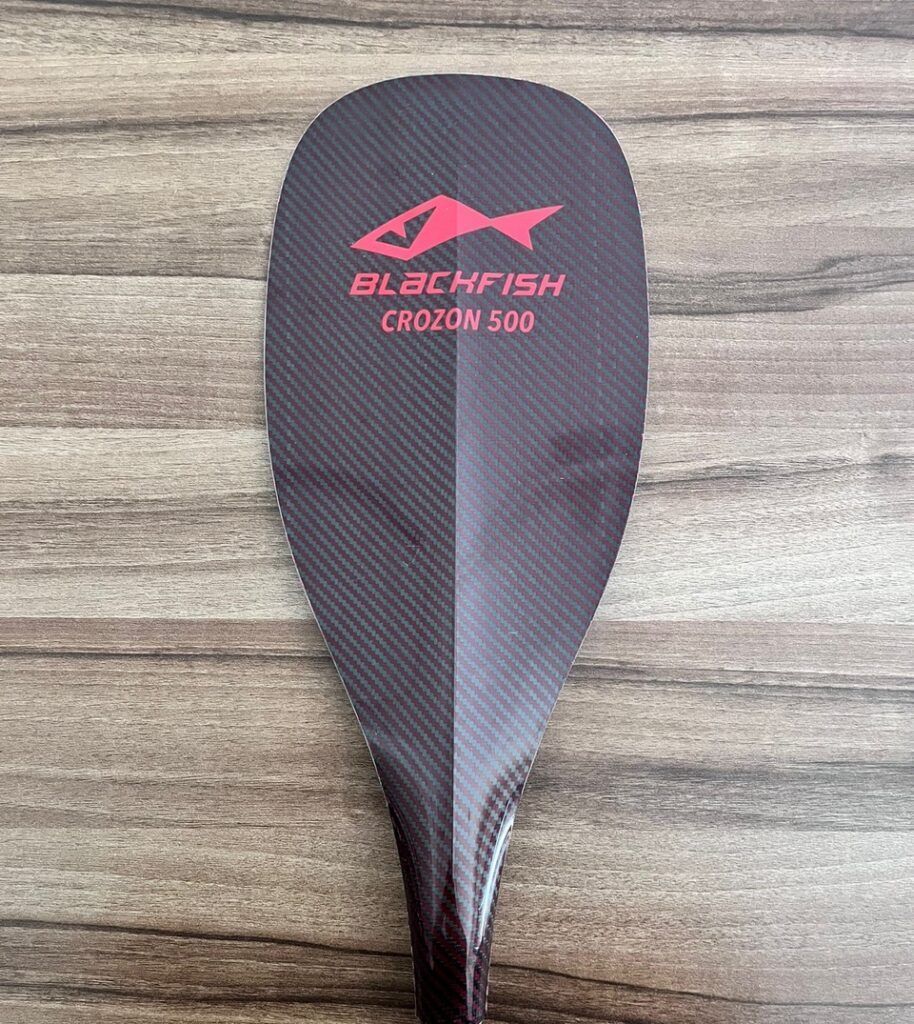 Blackfish Carbon 300 paddle blade on a wood surface, black with pink logo text