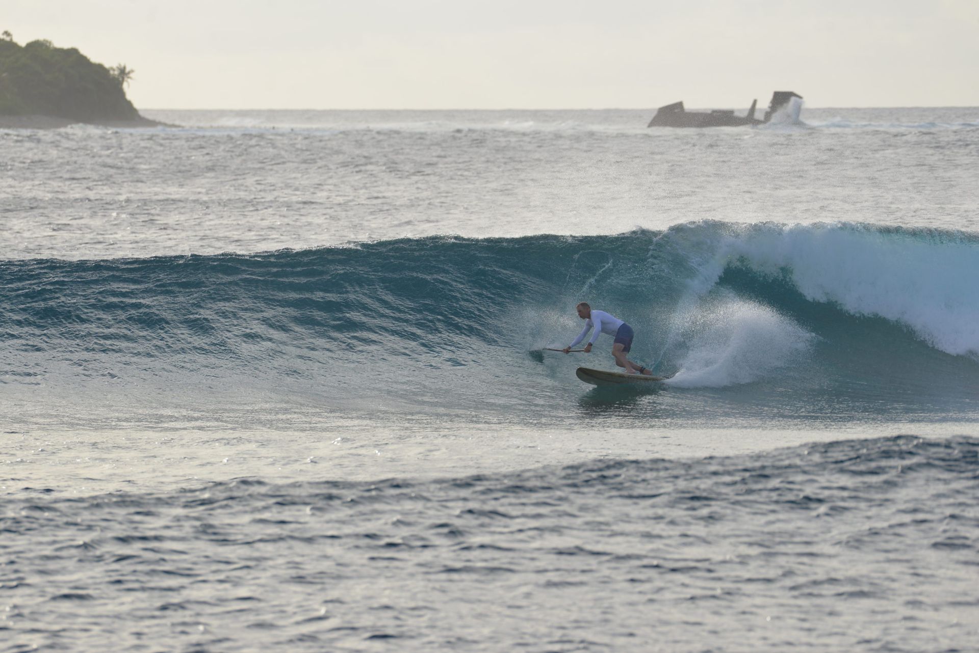 Surfer riding a blue wave near a rocky coastline at sunset