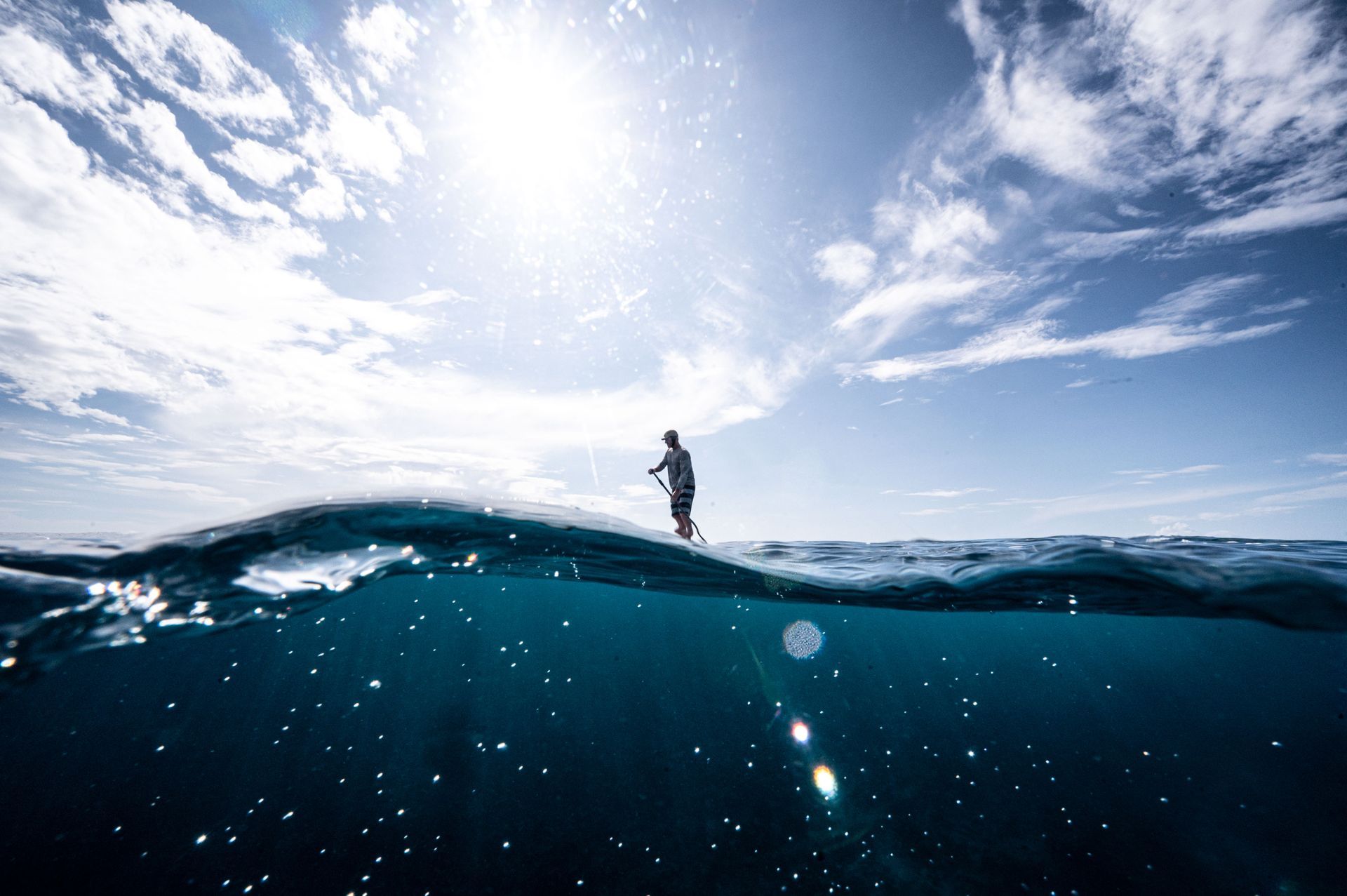 Lone surfer silhouetted on a wave under a bright sun and blue sky