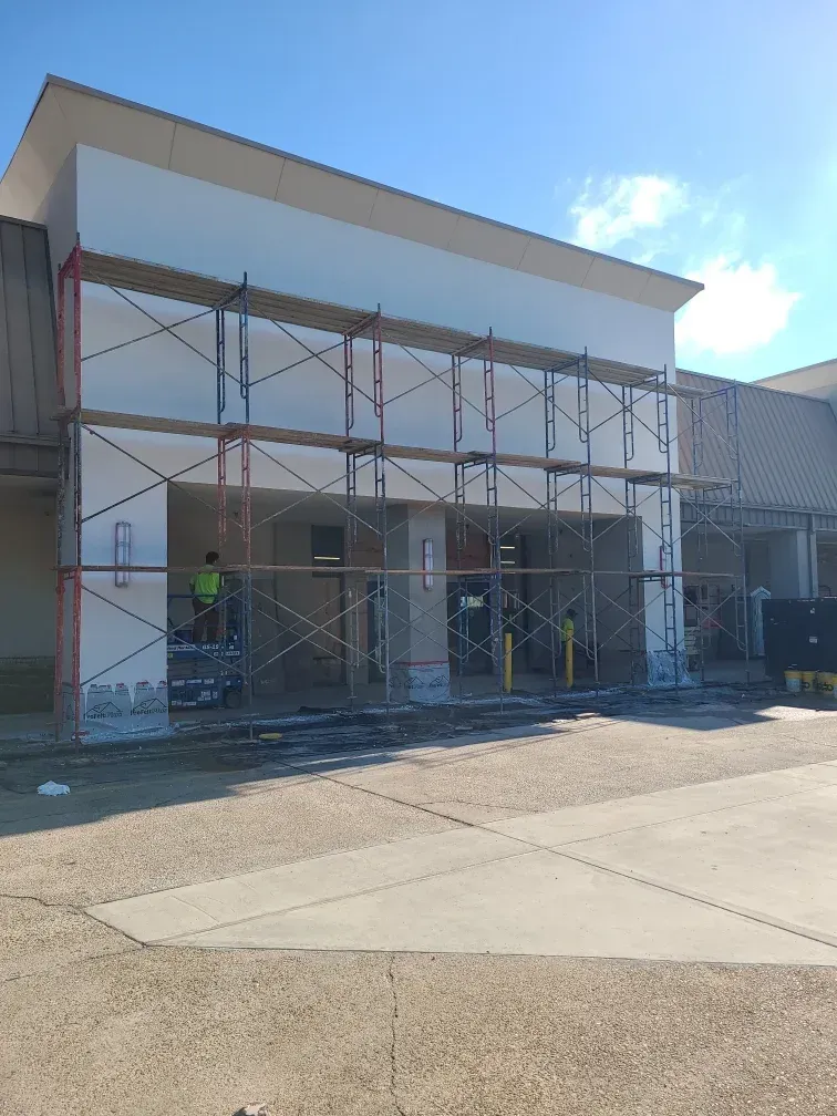 Construction scaffolding in front of a building entrance with a worker. Gray concrete and white facade.