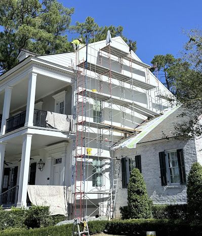A tall scaffolding structure stands against the white exterior of a two-story house undergoing maintenance.