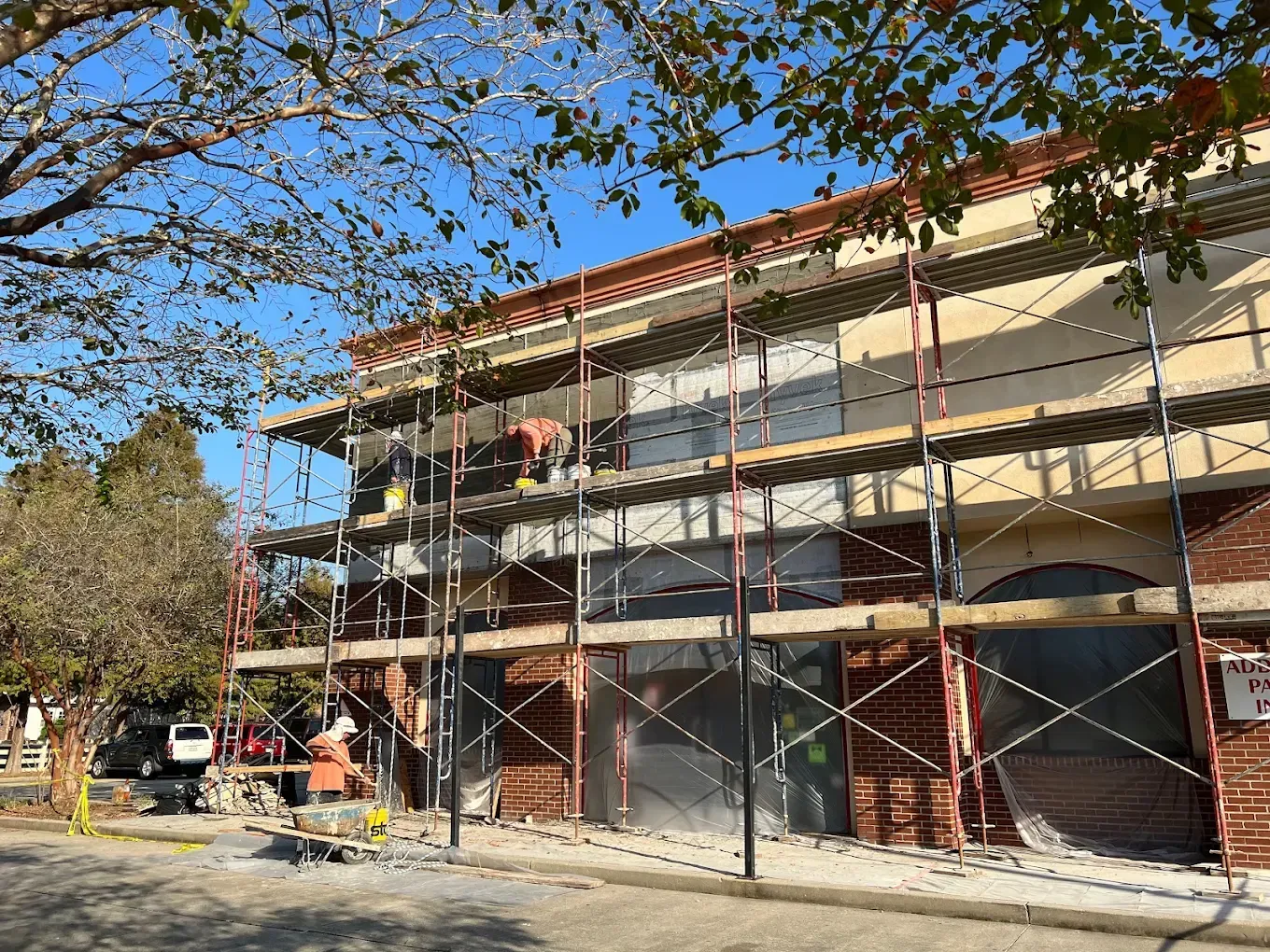 Building under renovation, scaffolding erected, brick facade, blue sky, tree branches.