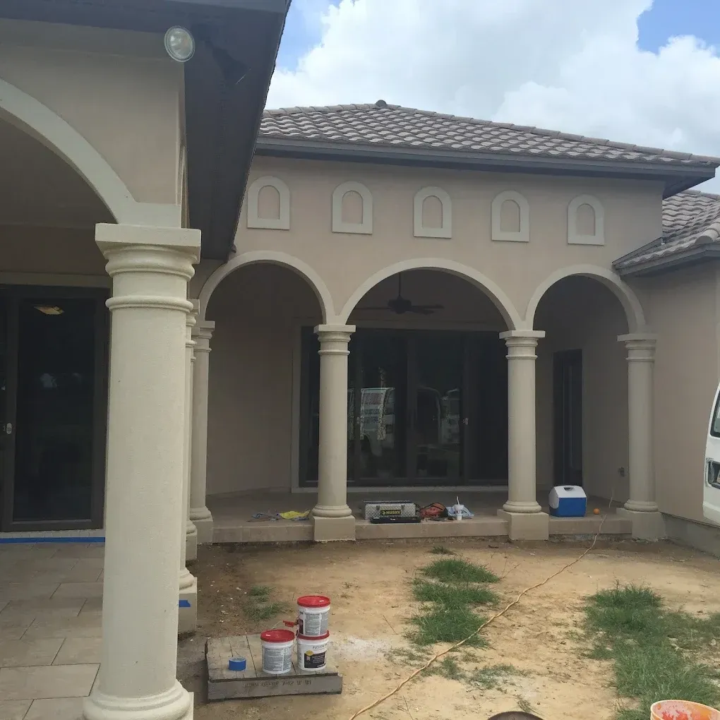 Beige stucco home with arched columns, patio area, and paint buckets.