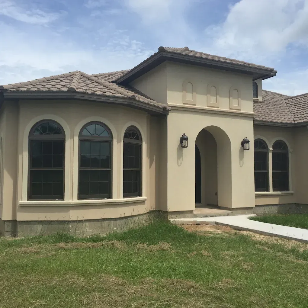 Tan stucco house with arched windows and entryway under a blue sky.