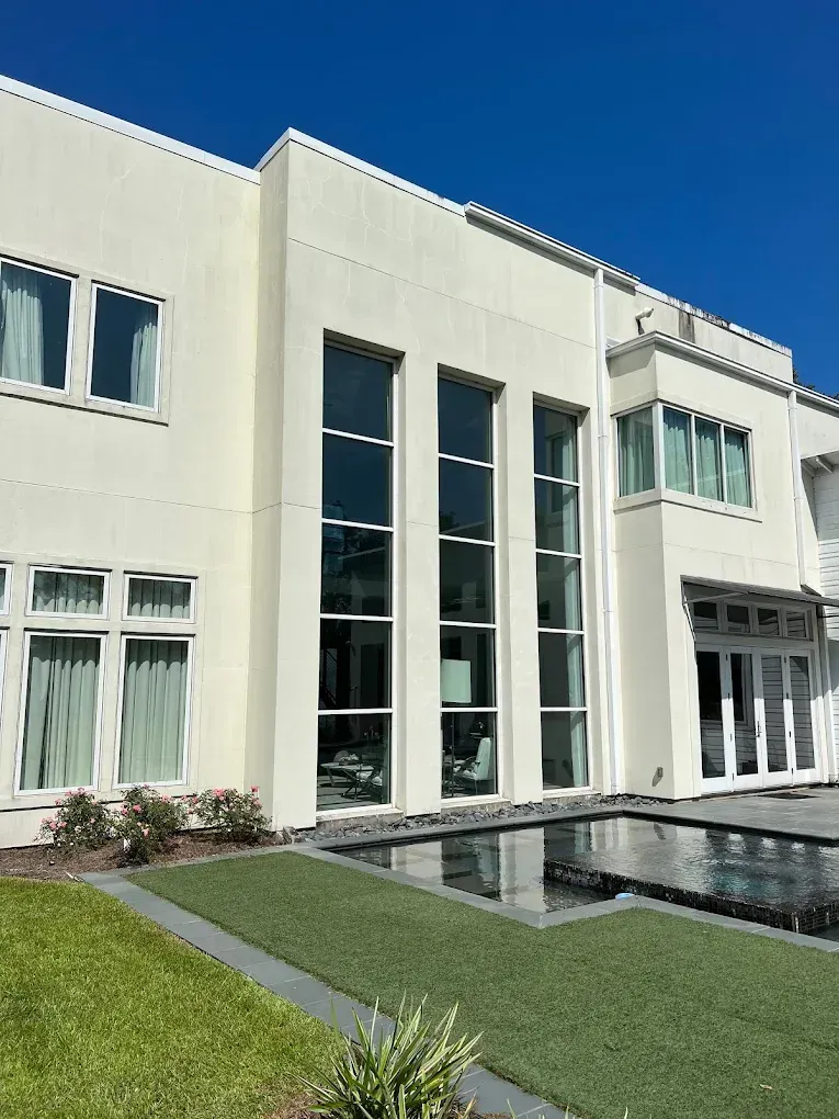Beige modern building with large windows next to a reflecting pool on a sunny day.