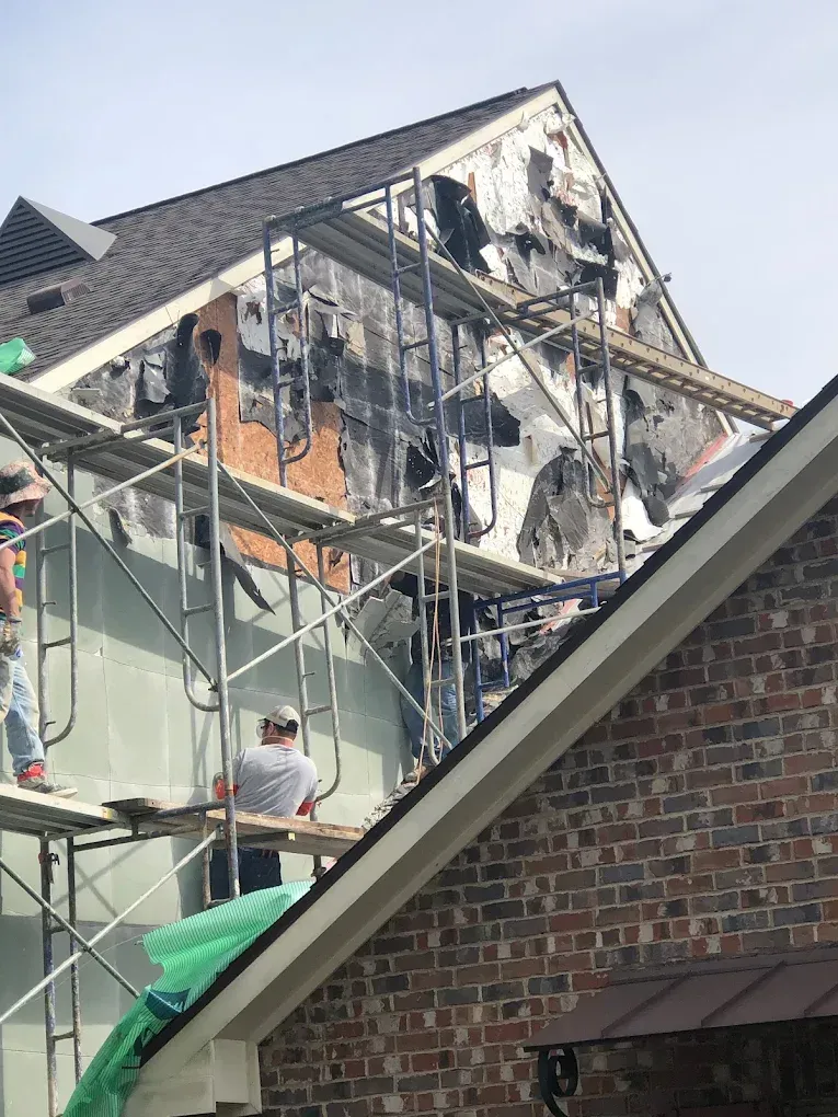 Scaffolding on a building with fire damage to siding; workers visible.