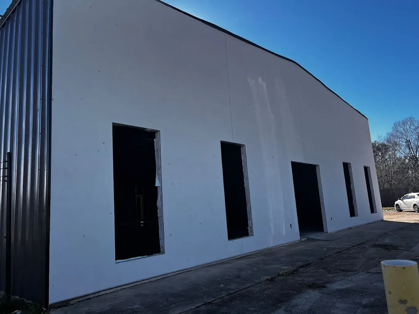 White industrial building exterior with dark window openings, under a clear sky.