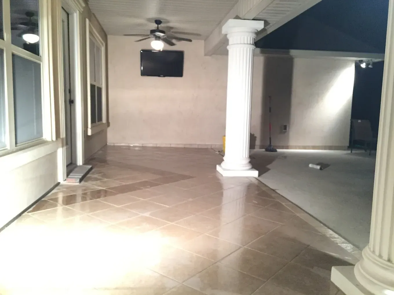 Covered patio with tile floor, TV, ceiling fan, and white columns.