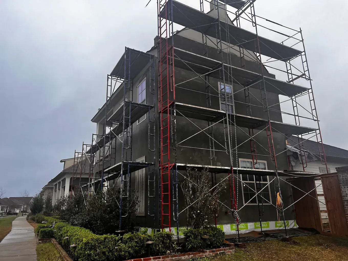 Building exterior under construction; scaffolding, black siding, cloudy day.