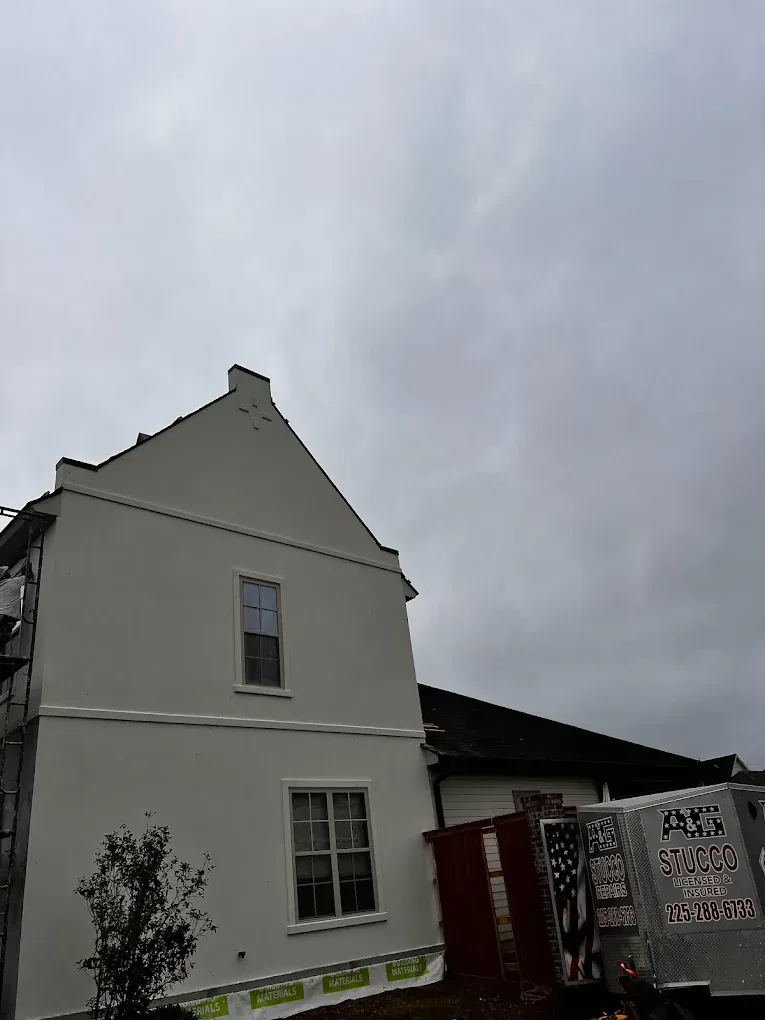 White house exterior against cloudy sky. Two windows visible on the facade, with a partially visible delivery truck.