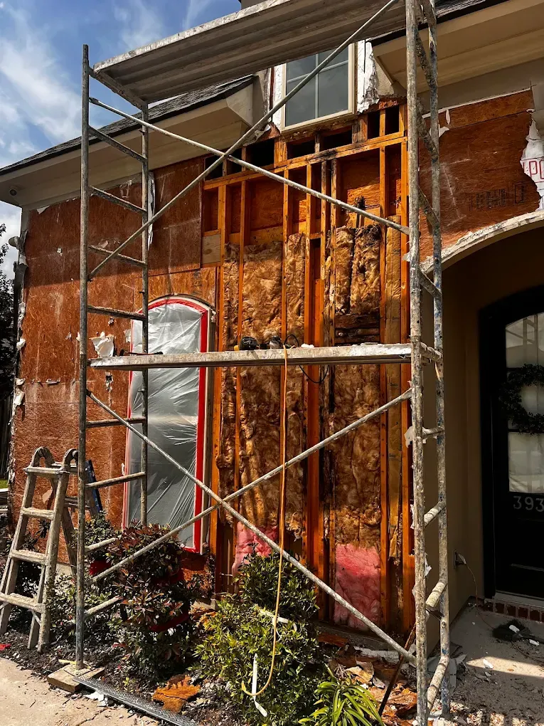 Exterior wall construction: scaffolding, exposed wood framing, insulation, and removed stucco.
